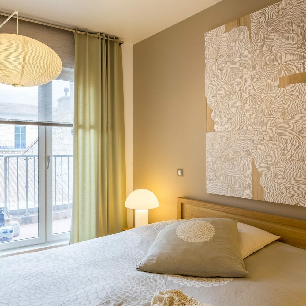 Chambre lumineuse avec lit en bois, luminaire suspendu et décoration florale murale