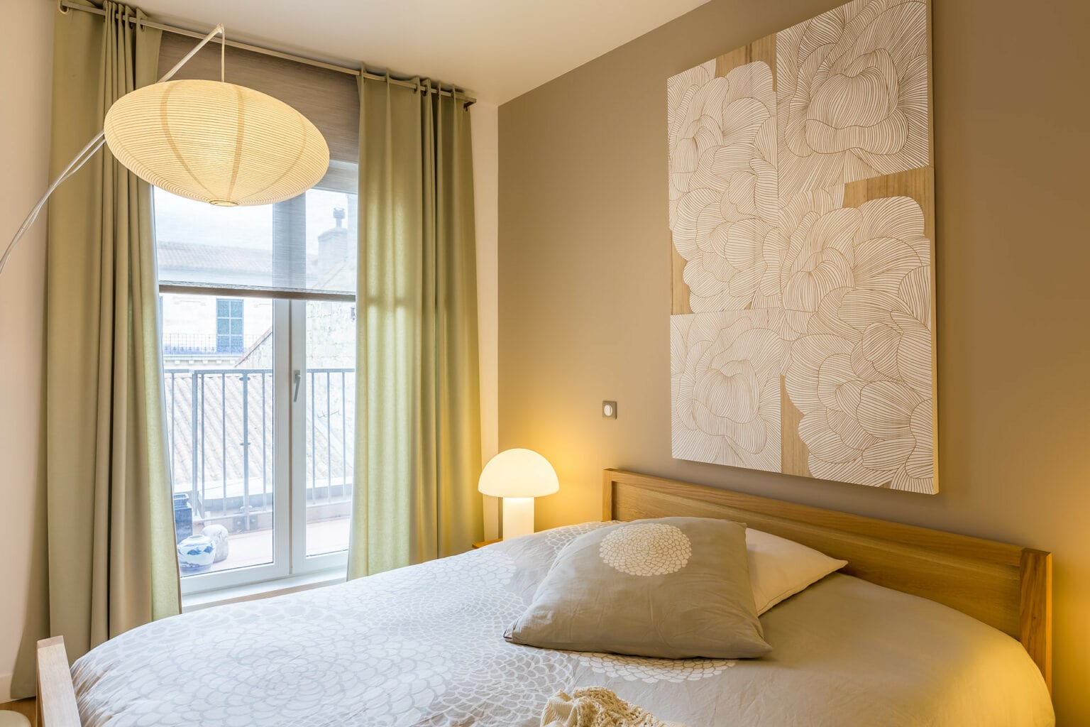 Chambre lumineuse avec lit en bois, luminaire suspendu et décoration florale murale