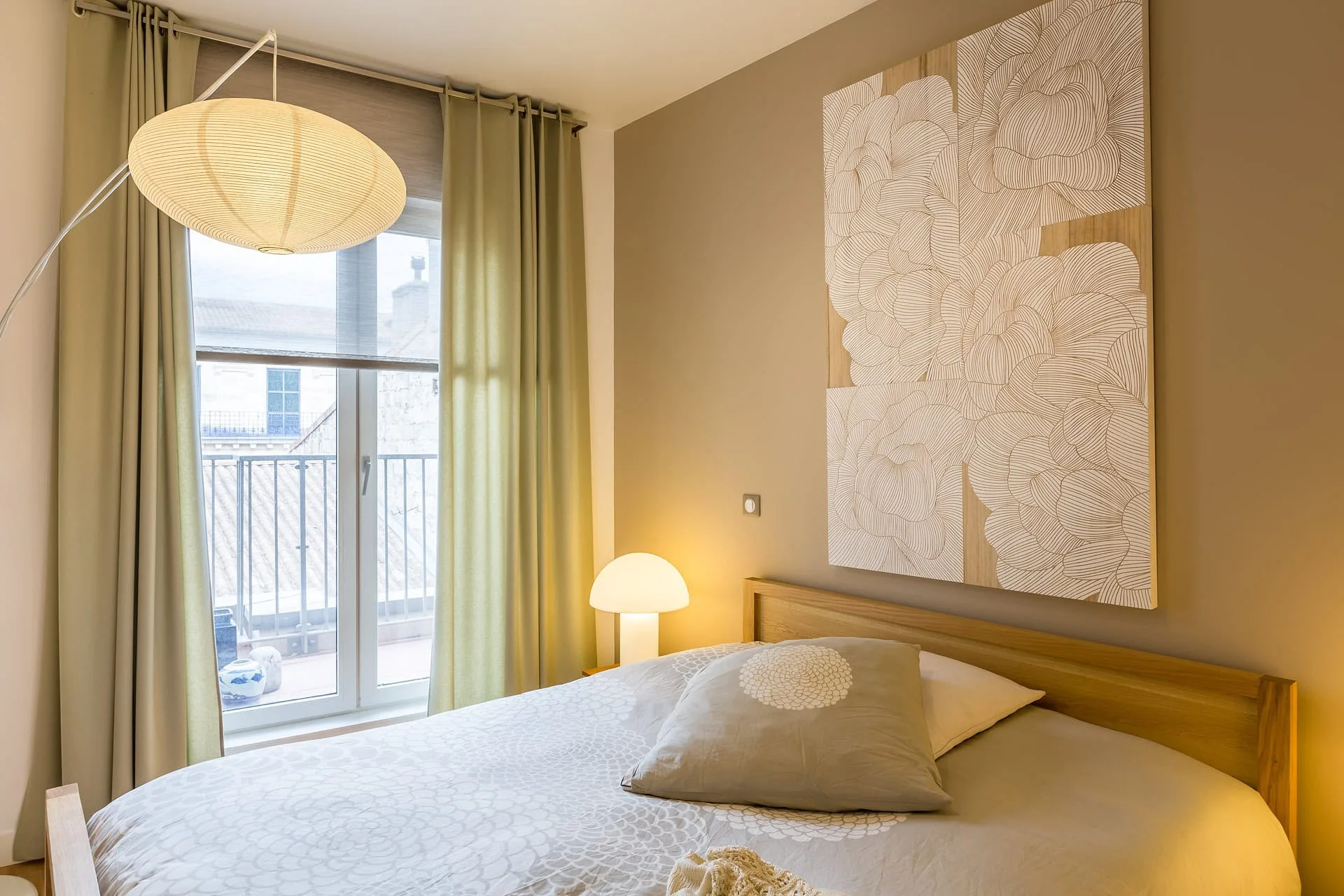 Chambre lumineuse avec lit en bois, luminaire suspendu et décoration florale murale