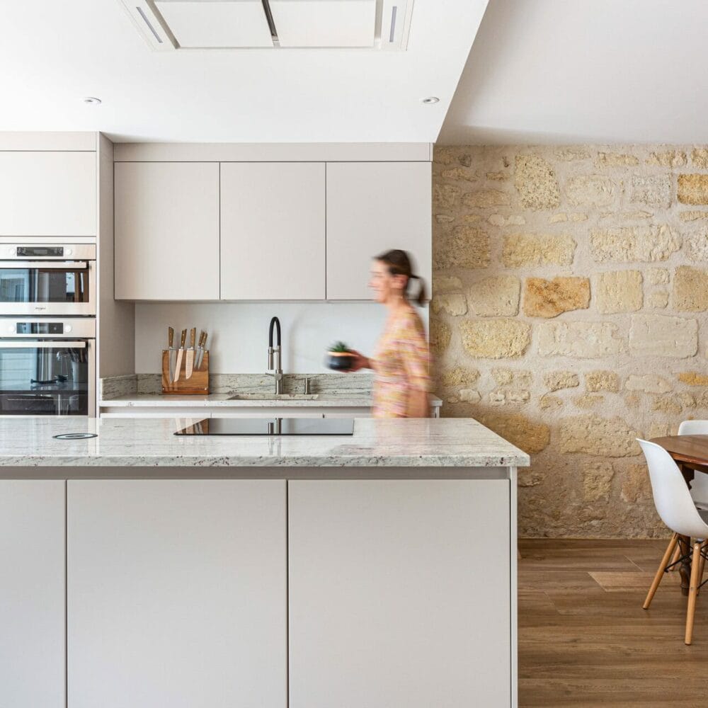 Cuisine avec îlot en marbre et mur en pierre donnant sur une salle à manger au design épuré.