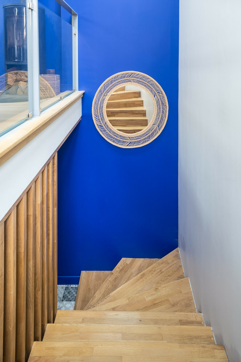 Escalier en bois avec miroir rond en rotin et mur bleu vibrant pour une touche moderne
