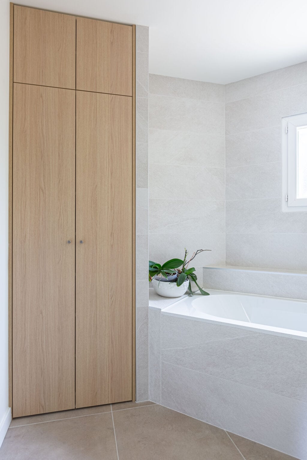 Salle de bain épurée avec baignoire encastrée, meuble vasque en bois et murs carrelés en faïence claire.