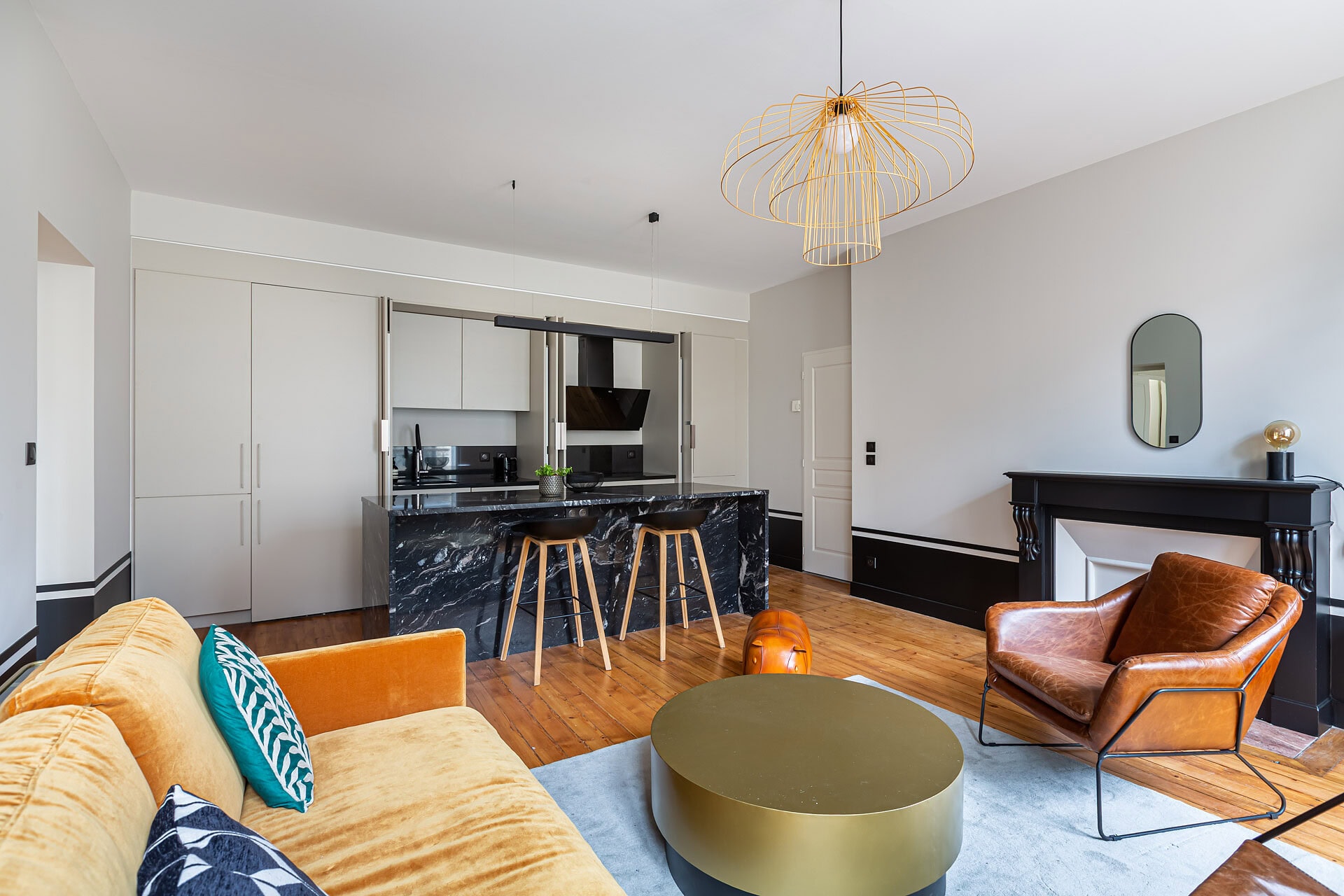 Salon avec cuisine ouverte, îlot en marbre noir, canapé en velours jaune et fauteuil en cuir marron